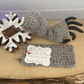 A pair of gray, speckled fingerless wrist warmers displayed on a wooden surface with a 'Let it Snow' snowflake decoration in the background.