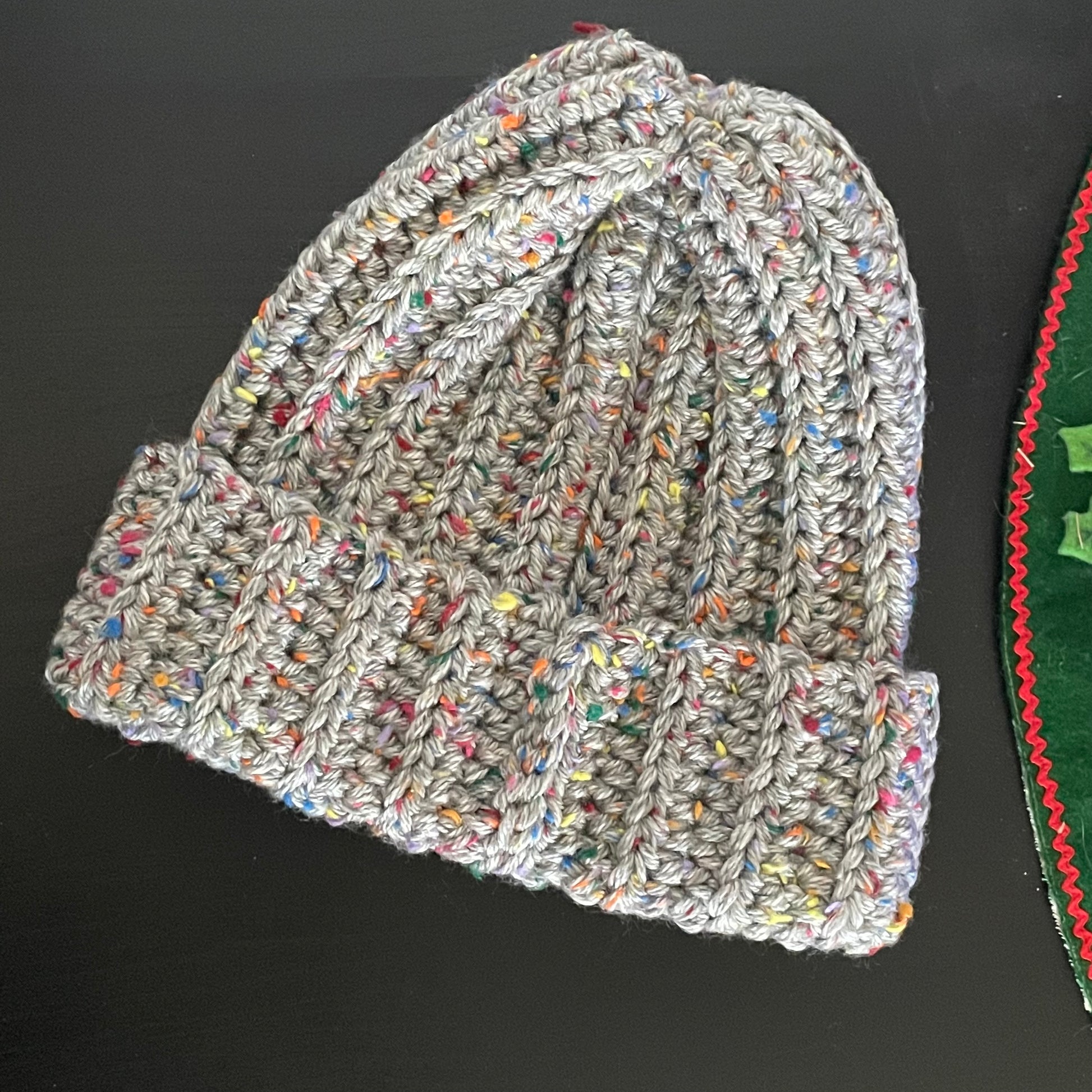 Extra Warm Ribbed Cable Knit Hat Silver & Speckled Rainbow Hand Crocheted Beanie Winter Unisex Outdoor Stretch Adjustable Cuff displayed flat on black table