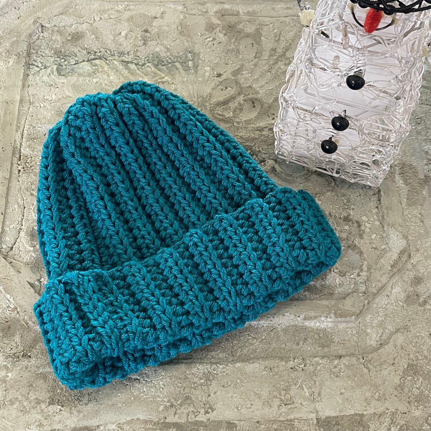 Extra Warm Ribbed Cable Knit Hat Solid Blue Green Hand Crocheted Beanie Winter Unisex Outdoor Stretch Adjustable Cuff displayed flat on stone background